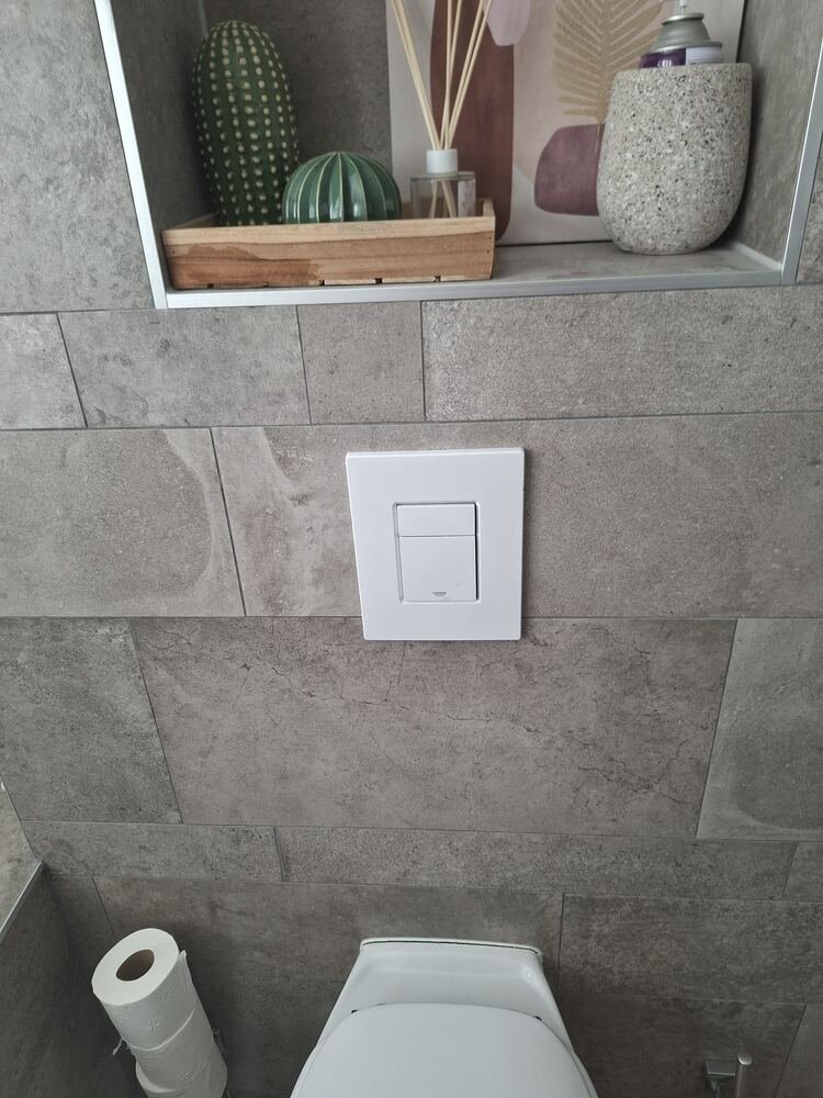 Strakke witte Grohe bedieningsplaat op een betegelde toiletwand