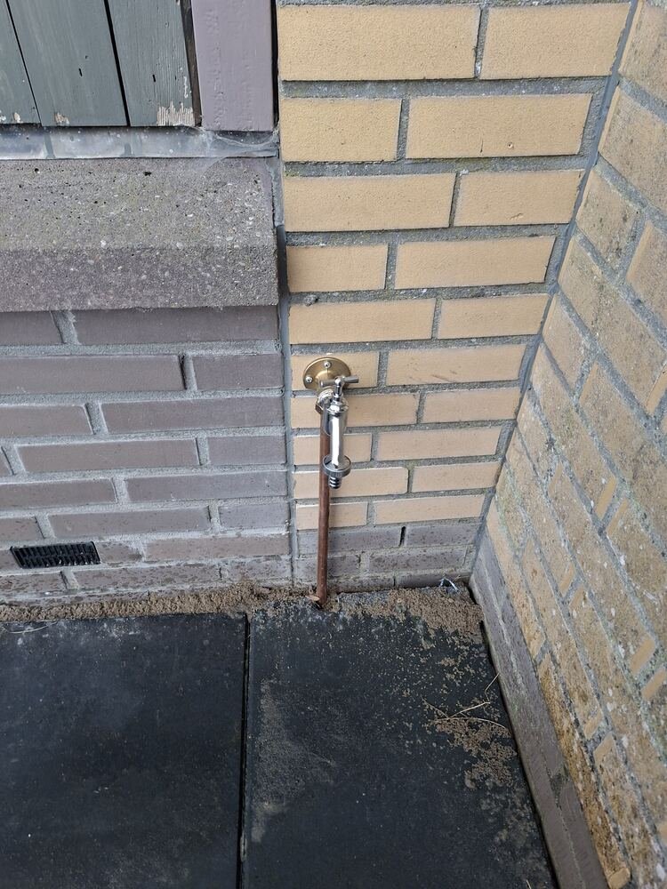 Nieuwe buitenkraan met koperen leiding netjes weggewerkt in de hoek van een gevel