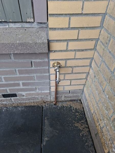 Buitenkraan met koperen leiding in een gevelhoek