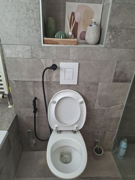 Toilet met zwarte bidetsproeier en Grohe bedieningsplaat in een betegeld toilet
